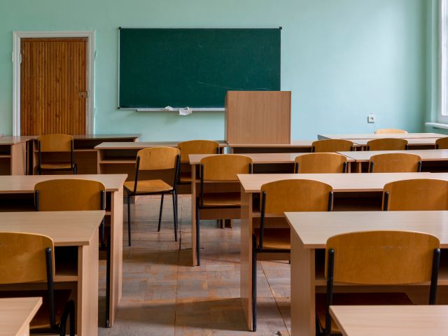 A bright classroom lined with wooden desks and chairs